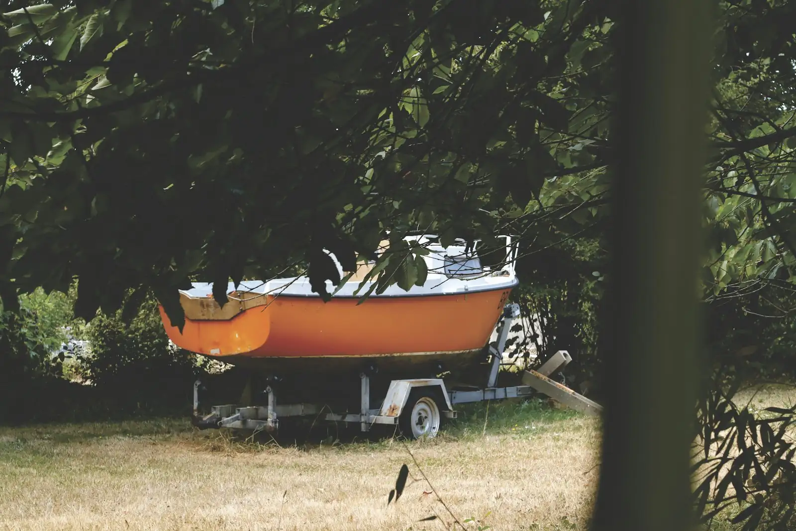 An orange boat on its trailer, parked on the grass in a backyard