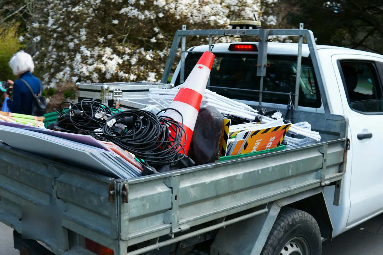 A white work ute with a tray full of cables, signs and a traffic cone