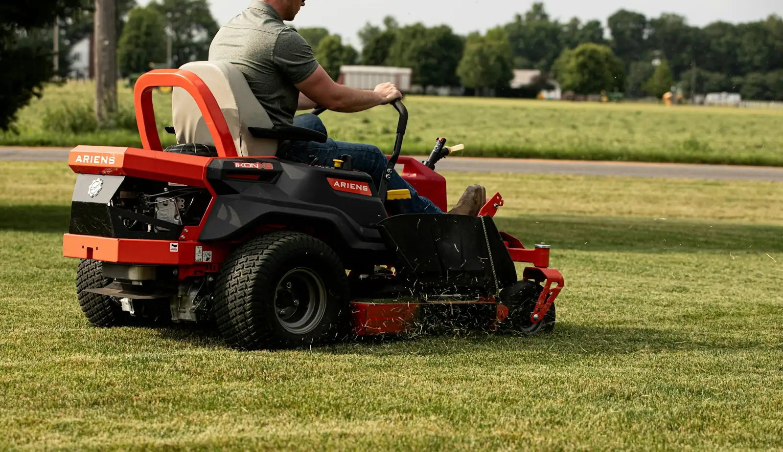 A man mowing a large lawn on a red zero-turn mower