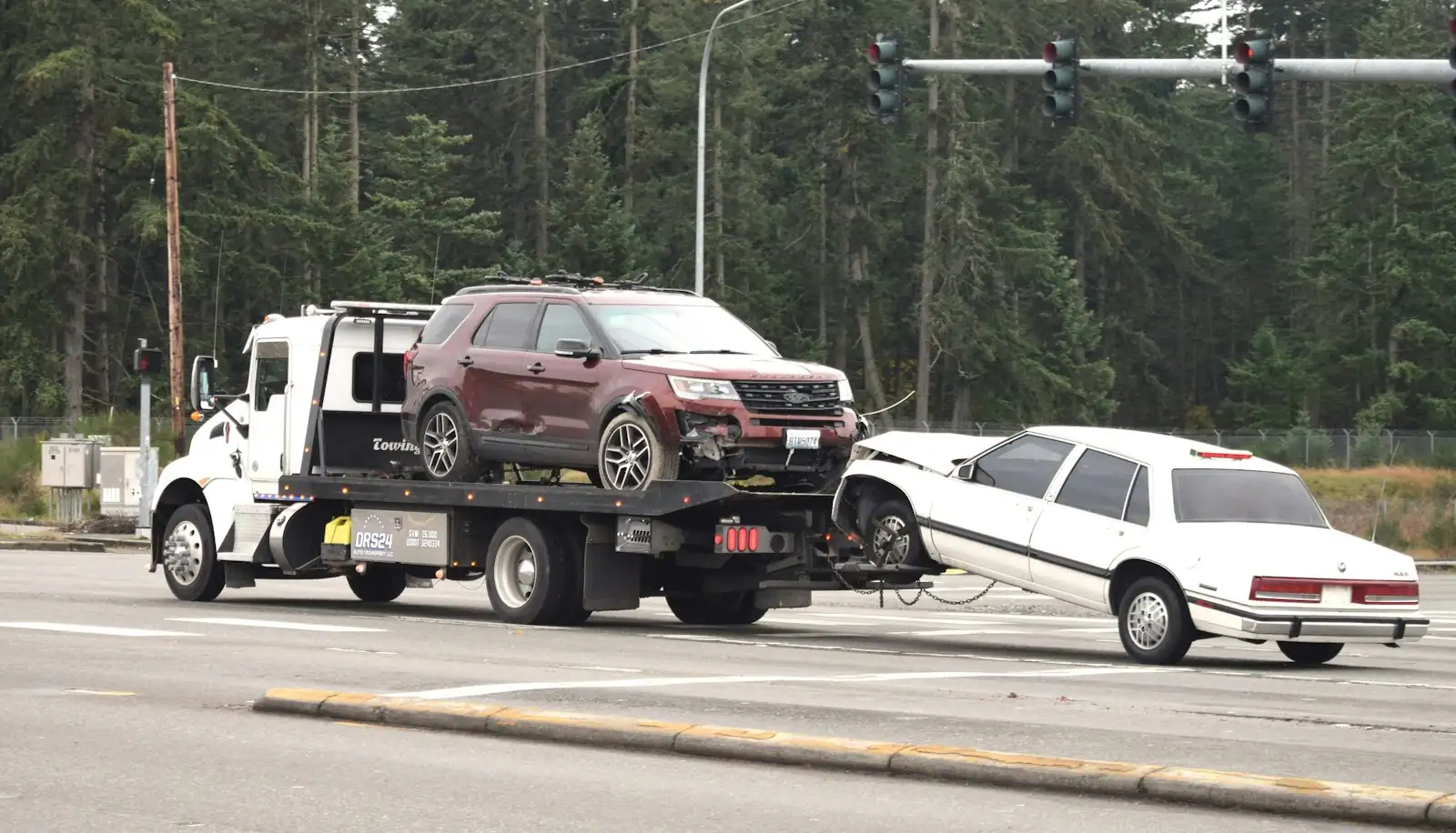 A tow truck carrying a car on its tilt tray along a road